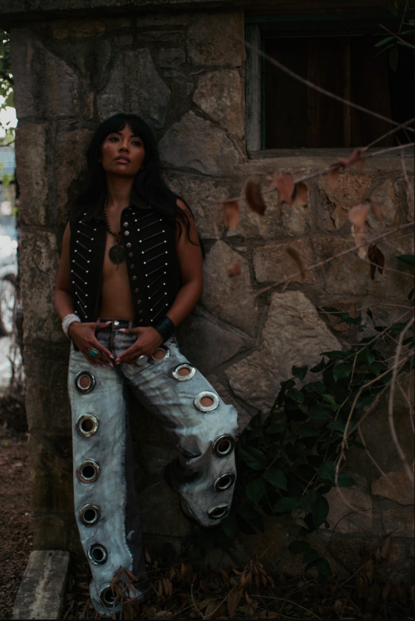 Person wearing a unique outfit with decorative elements against a stone wall.