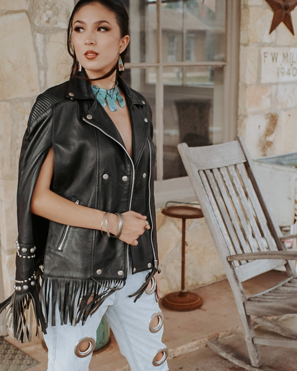 Woman wearing a black leather vest with fringe in a rustic setting