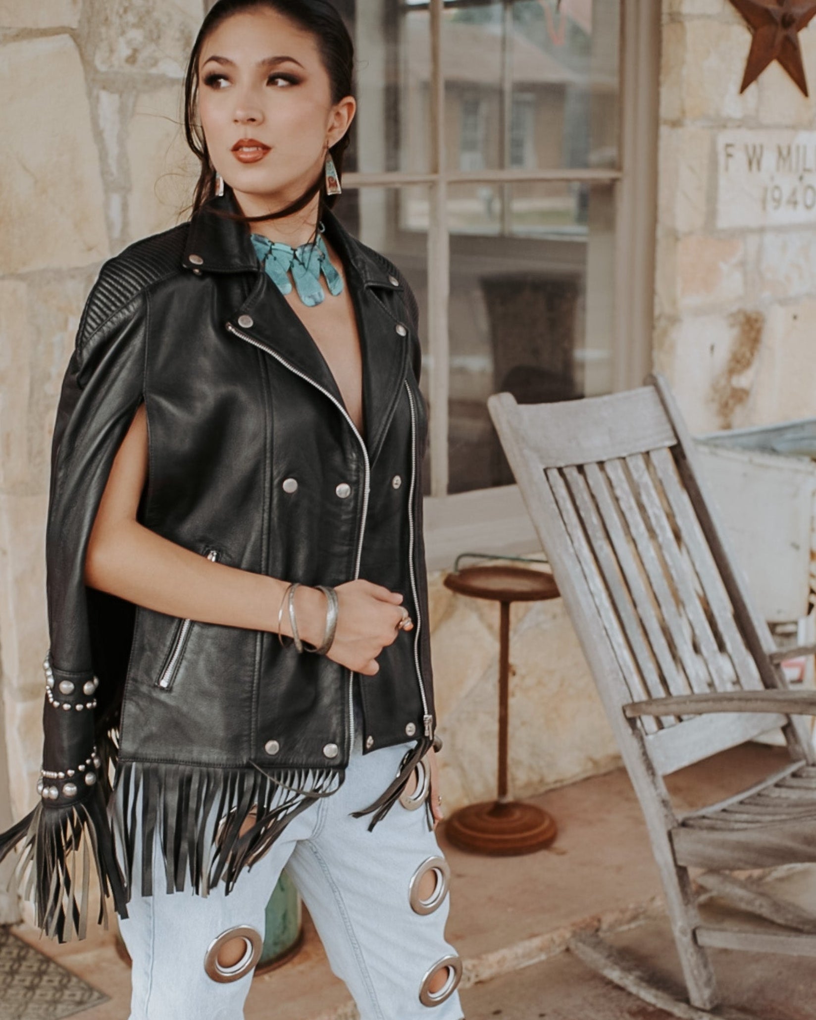Woman wearing a black leather vest with fringe in a rustic setting